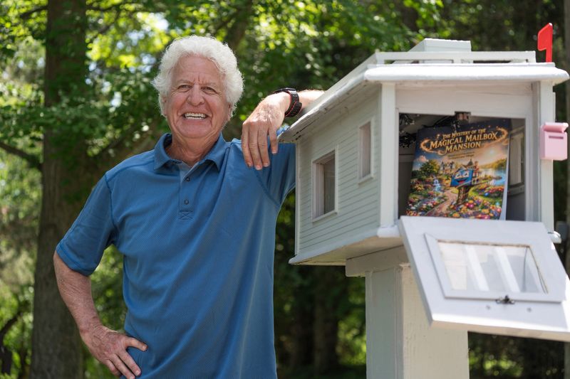 Don Powell, of Orchard Lake, stands with the children’s book he made about a doll family who moved into his custom-made mailbox at his home on Thursday, June 11, 2026. The story generated national interest.