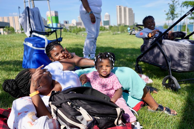 The Mathis family tries to stay cool under a tree at a ticketed event at Ralph C. Wilson, Jr. Centennial Park in Detroit for the 2026 Ford Fireworks along the Detroit river.