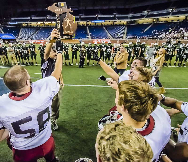 Portland Head Football Coach John Novara holds the Division 5 State Championship trophy as members of his team move in to celebrate Saturday November 24, 2012 at Ford Field in Detroit.