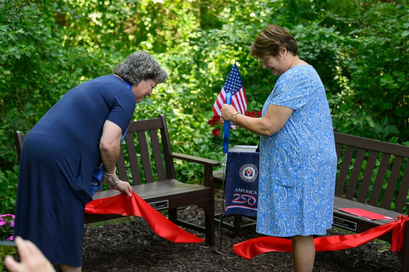DAR members Tracy Fischer, left, and Lauren Smith cut a ribbon to open two benches during a ceremony held by two chapters of the Daughters of the American Revolution, at Fisher House, in Ann Arbor, July 8, 2026.