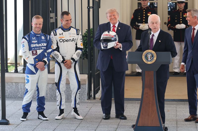 At the Freedom 250 Grand Prix West Wing preview in Washington, D.C., Felix Rosenqwist, Alex Palou, and Roger Penske give President Trump a racing helmet.