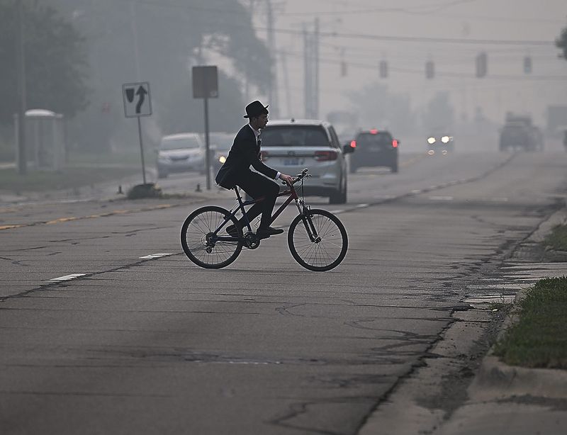 A man rides his bike across a 10-mile road near Greenfield Road while the smoke from the wildfire lingers in the background on Thursday, July 16, 2026, in Southfield, MI.