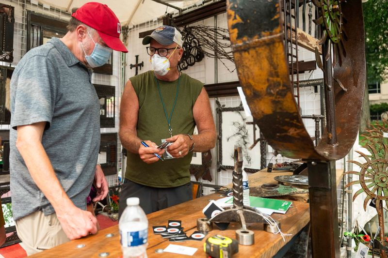 Richard Morgan, right, chats with Dan Meehan of Ohio, left, after Meehan purchased one of Morgan’s sculptures during the annual Ann Arbor Art Fair on Thursday, July 16, 2026 in Ann Arbor, Mich. Some visitors to the annual event wore masks to protect themselves from the heavy smog caused by Canadian wildfires.