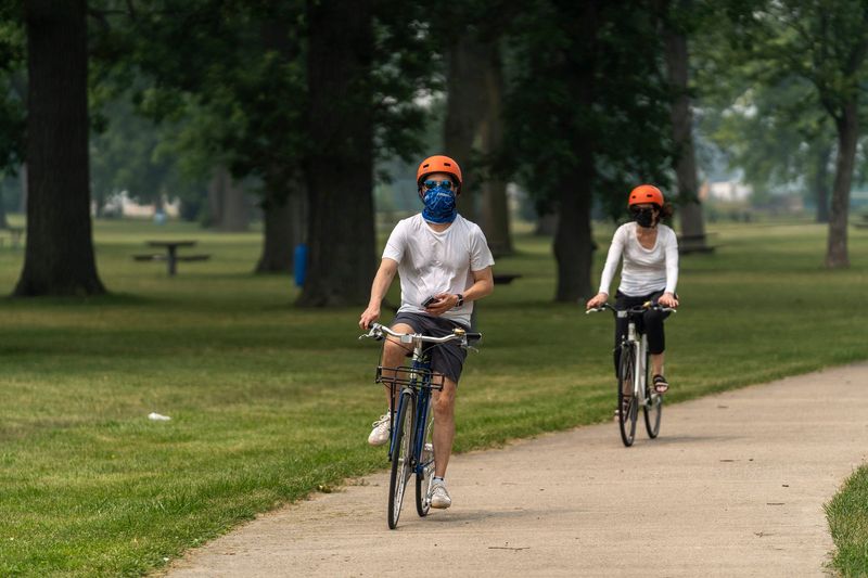 Bicyclists wearing face coverings ride along a path on Belle Isle as wildfire smoke hangs over Detroit on Friday, July 17, 2026.