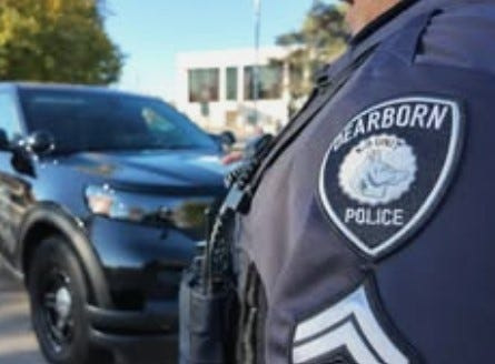 A Dearborn police officer stands in front of a patrol vehicle.