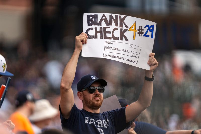A Detroit Tigers fan holds a handmade sign offering a blank check to Tigers pitcher Tarik Skubal (29) during a game against the Baltimore Orioles at Comerica Park in Detroit on Wednesday, July 29, 2026.