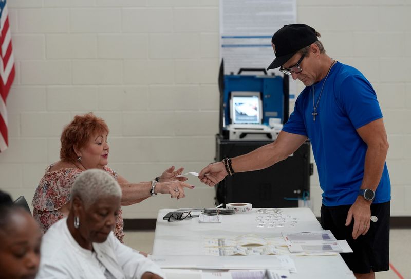 Christopher Bahrke, 55, of Pontiac hands in his voting ballot tear off tab to an election worker before feeding the ballot into the nearby machine at precinct 4 inside of the Robert Bowens Senior Center in Pontiac on Tuesday, August 4, 2026.