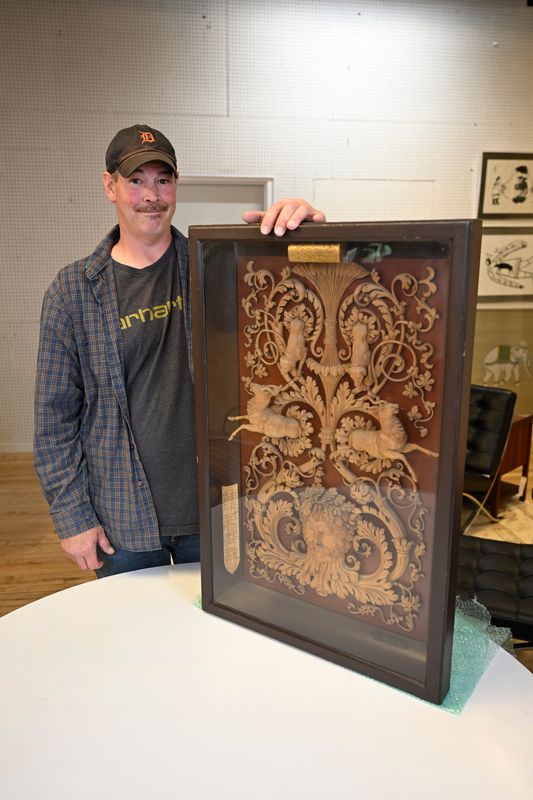 John Thomson of Berkley stands with a framed display of a wood carving from 1825, Tuesday, June 16, 2026, at DuMouchelle Art Gallery in Detroit.