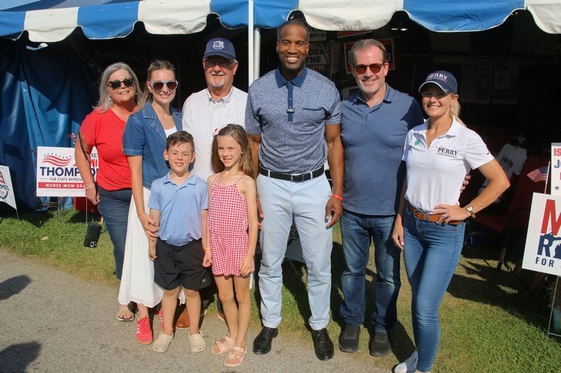 L to R: Reda Benicki, Hannah Loop, her children Fin and Liberty, Dale Benicki, John James, Randy Richardville, and Laura Perry stand in front of the GOP tent at the Monroe County Fair.