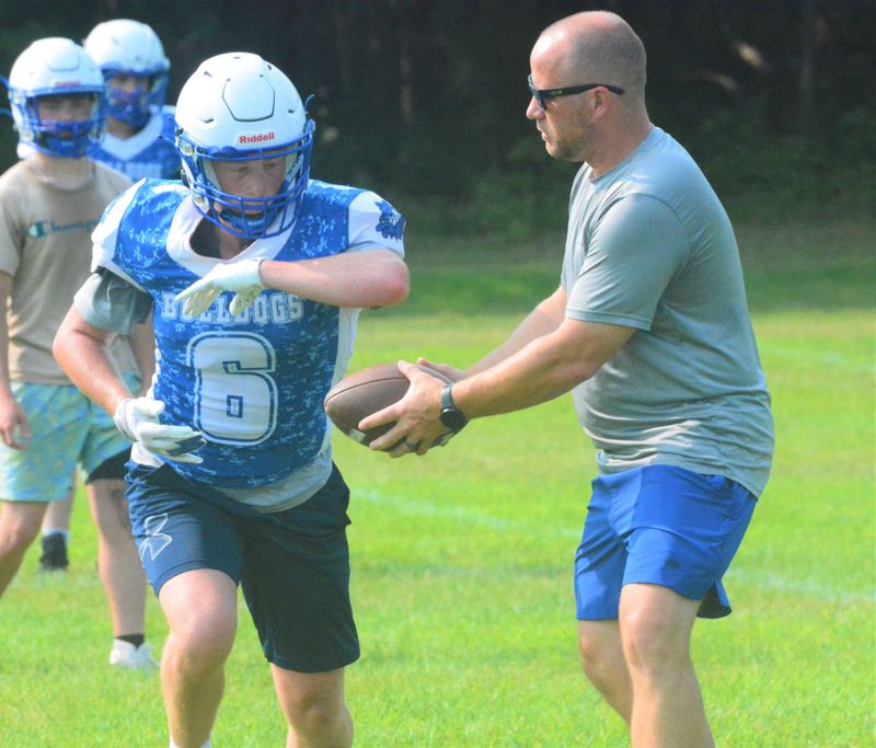 Inland Lakes senior Elijah Perkins (6) takes a handoff from head coach Travis Meyer during a football practice on Wednesday, Aug. 12. The Bulldogs will compete in football-only Bridge Alliance Conference Straits Division this fall.