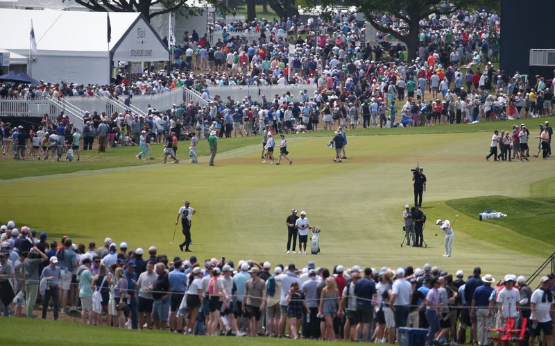 Surrounded by a massive gallery of fans, Rory McIlroy, bottom right, hits his second shot from the fairway to the green on the 1st hole during the final round at the PGA Championship at Oak Hill Country Club Sunday, May 21, 2023.