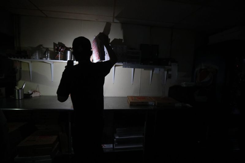 High winds have caused power outages in the North Chili, NY area with several traffic light out, like the one at Westside Drive and Union Street on December 11, 2021.  Towne Plaza was also without power.  An employee, at Pizza 151, using his cell phone's flashlight pulls some pizza boxes out to box the orders that were complete.