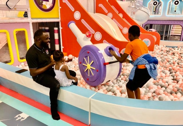 Foluso Odeyale, owner of The Fun House at The Mall at Greece Ridge, looks on with his daughter, Olamide, 3, while his son, Ayomide, 9, launches a ball from a toy cannon. Odeyale, a Henrietta resident, originally is from Nigeria.