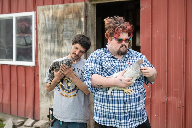Ryan Bushway, left, and his brother Cody Bessette hold chickens on their family farm on Glass Road in Champlain, New York, on May 13, 2025. They live in the shadow of a border surveillance tower.