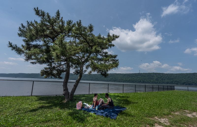 Lauren DeLucia and Derrick Celestine of Yonkers find a patch of shade under a tree as they spent part of a scorching hot day at the JFK Marina in Yonkers June 23, 2025. Over the next two days, heat index values are forecasted to reach 107 degrees as a heat wave envelops much of the East Coast.