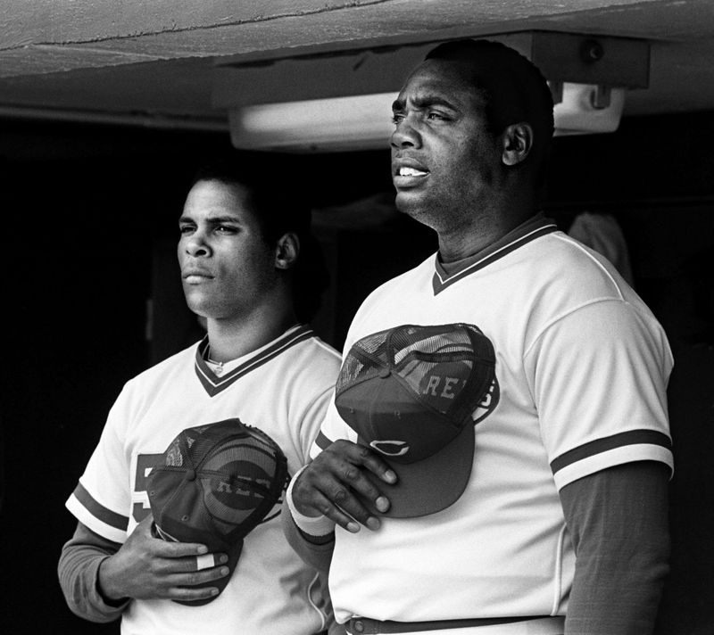Cincinnati Reds teammates Barry Larkin and Dave Parker (from left) stand for the national anthem before an exhibition game against the Montreal Expos in 1987. Parker, who died last month, will join Larkin in baseball's Hall of Fame with his induction Sunday in Cooperstown.