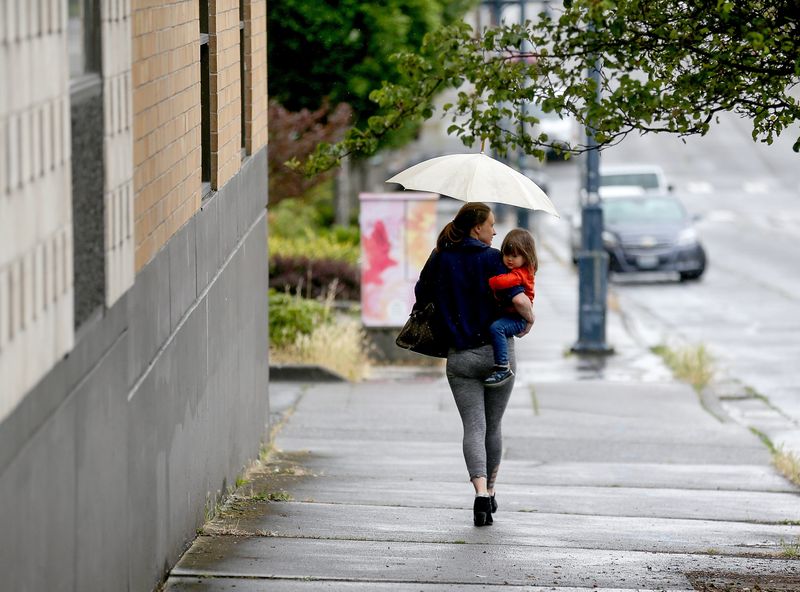 A person carries a child as they walk down 5th Street under an umbrella in Bremerton on a rainy Thursday, June 26, 2025.