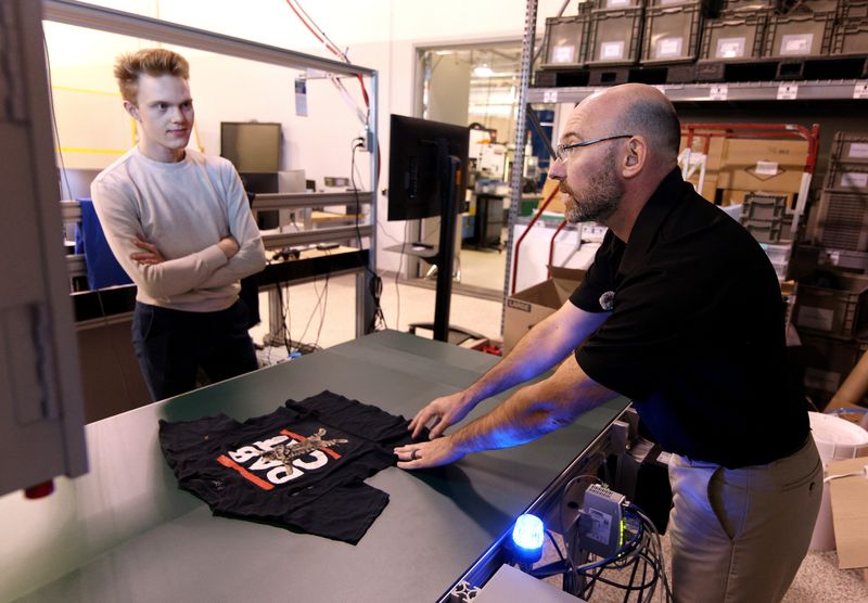 Mark Walluk, right, technical program manager, and Nick Spears, staff engineer, explain how the clothing dismantling project works at RIT. The system removes contaminants such as logos, elastic and zippers from clothing, so it creates a more pure material that can be used again.