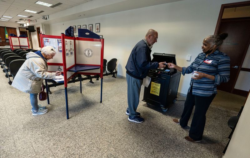 Poll worker Claudette Mills hands a sticker to Tom Bock of Greenburgh after Bock voted at Greenburgh Town Hall Nov. 4, 2025. At left, Susan Bock casts her vote.