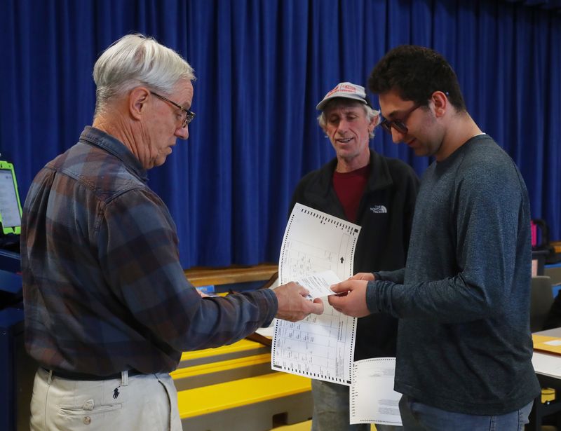Poll worker Doug Lyke hands James Reilly his ballot at Vassar Road Elementary School in the Town of Poughkeepsie on November 4, 2025. Reilly, a first time voter is joined by his grandfather, Larry.