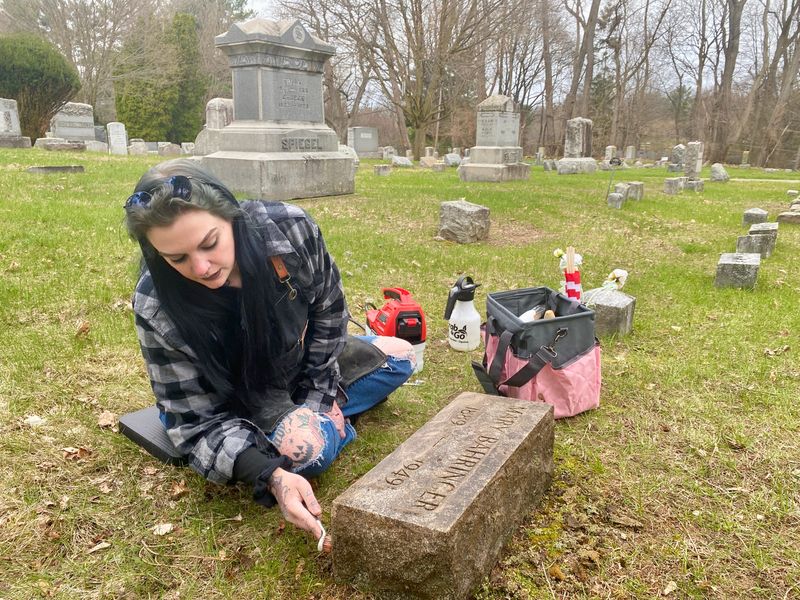 Stefanie Hohmann works to restore a headstone at Pittsford Cemetery on April 12, 2026. She joins a coalition of hobby preservationists that work to protect the historical artifacts from moss and lichen and bring new life to the names of people buried there.