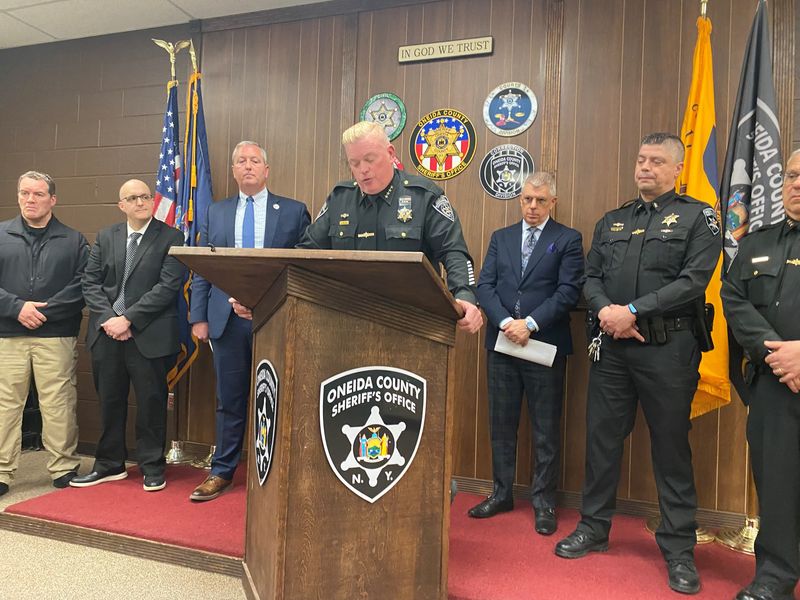 Oneida County Sheriff Robert Maciol, at podium, flanked by Oneida County Executive Anthony Picente Jr, to Maciol's left, Clinton Superintendent Christopher Clancy, to Maciol's right, and other law enforcement officers, speaks at a press conference on a foiled plot for a shooting at Clinton Middle School on April 13, 2026 in the Oneida County Sheriff's Office in Oriskany.