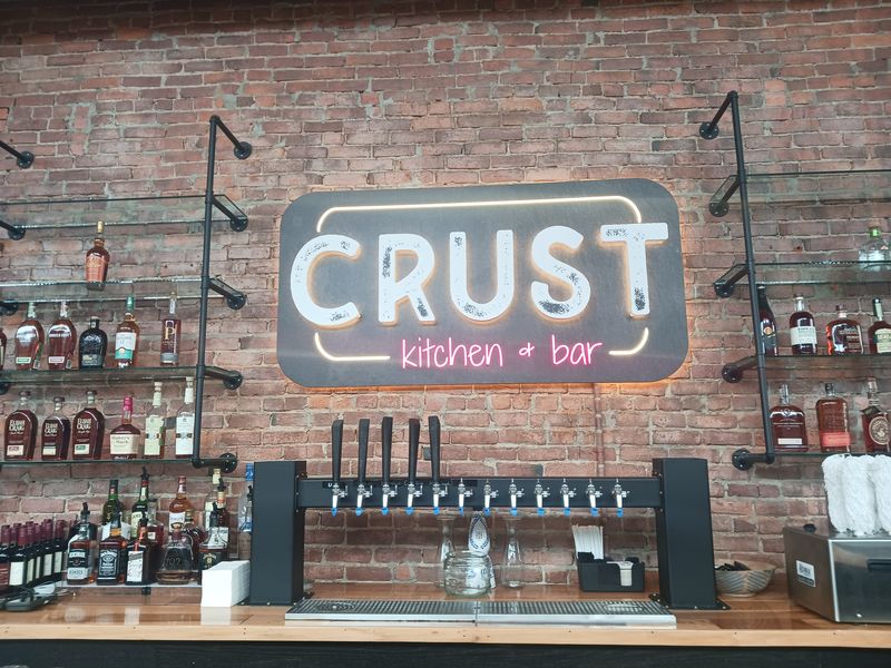 CRUST Kitchen & Bar sign hangs over the bar at new Utica location of popular Rome restaurant, preparing for grand opening Mon., May 11, 2026, 330 Main Street - across from Utica's historic Train Station.