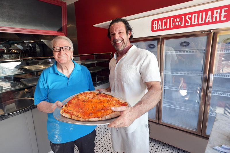 Chris Weisman, right, owner of Baci in the Square, and his former boss Gaetano Nardi, 93, hold the first pizza pie made by Nardi in the new pizzeria May 20, 2026 in Ardsley. Weisman said he learned how to make pizza at Nardi's pizzeria in Ardsley 35 years ago.