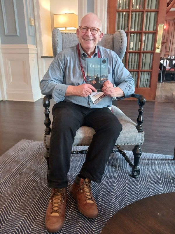 Author, Colgate University Alumnus Wayne Feinstein poses in the lobby of The Colgate Inn in the 'college town' of Hamilton holding a copy of "TURNING: a novel," his debut novel set to be released by Greenleaf Book Group Press on June 9.