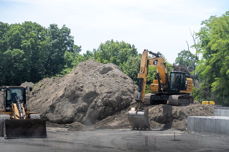 An excavator sits on a mound of dirt, next to a bigger mound of dirt, at the Penny Lane construction project in Warren on June 5.