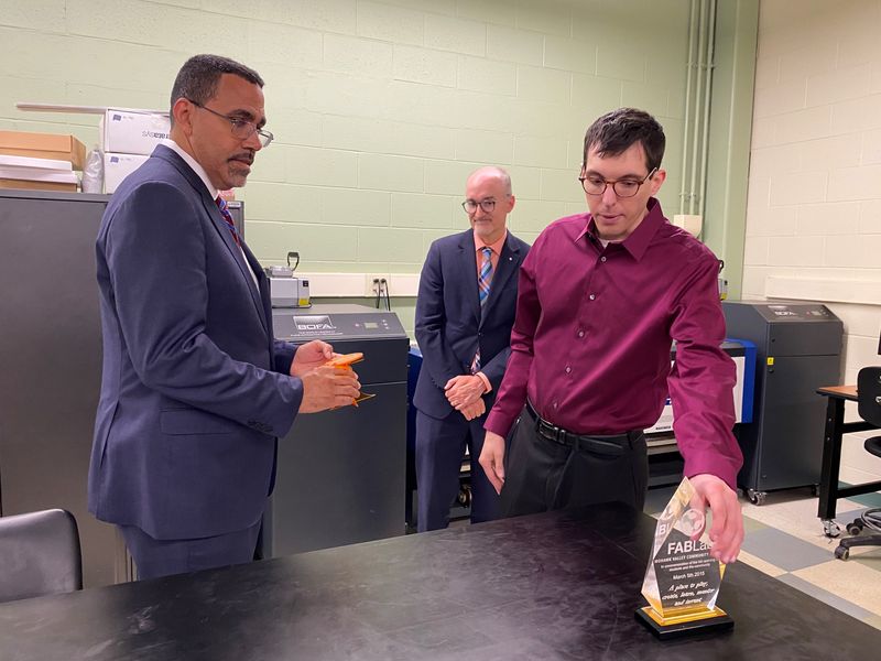 SUNY Chancellor John B. King, left, chats in the FABLab on Mohawk Valley Community College's Utica campus with a faculty member and MVCC President Randall VanWagoner, middle, about an award and other items made in  in the FABLab on June 24, 2026. King stopped by the campus as part of a tour off all community college campuses to promote the SUNY Reconnect program for adult learners.