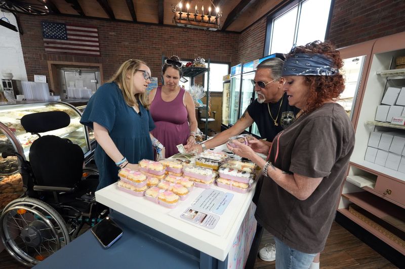 Laura Timmons looks on as her daughter Theresa Timmons, 18, sells mini cakes at her Sweet T's bakery pop-up at Homestyle Bakery, her family's bakery in Peekskill June 30, 2026. Theresa was in a car accident over two years ago and suffered a traumatic brain injury. She has since relearned to walk and talk, and recently launched this business during her recovery journey.