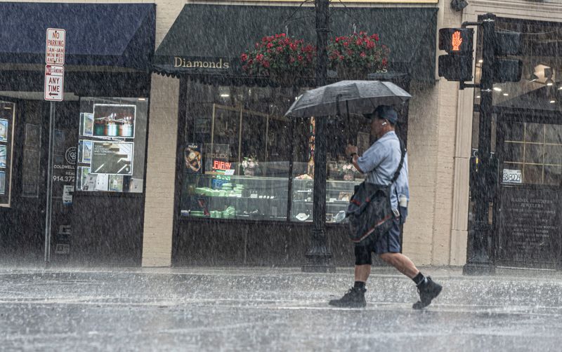 A postal worker walks through a heavy downpour as he crosses Main Street and North Broadway in Tarrytown July 21, 2026.