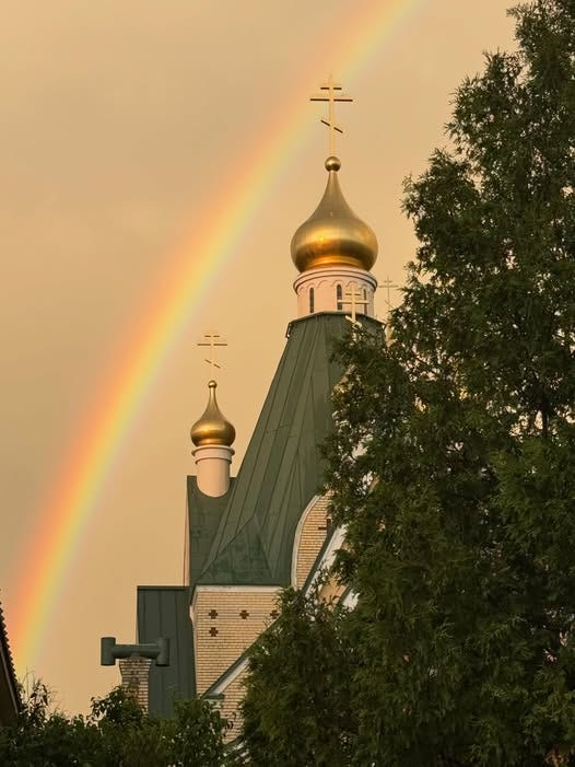 The golden onion domes and crosses of the cathedral at the Holy Trinity Monastery in Jordanville peak through the trees under a rainbox in tihs photo from the monastery's Facebook page.