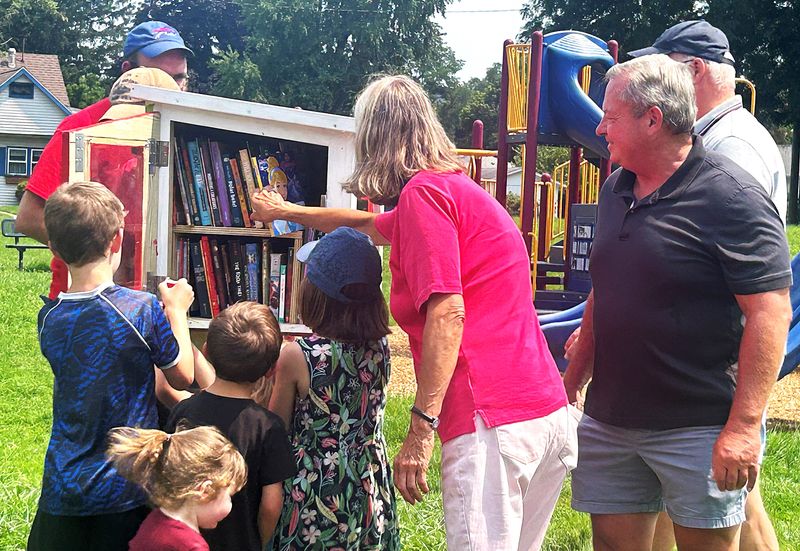 Elmira Mayor Dan Mandell, right, looks on as children choose books from the Family Reading Partnership of Chemung Valley's new Bright Red Bookshelf at Miller Pond Park. The bookshelves provide children with free books that they can take home and keep.