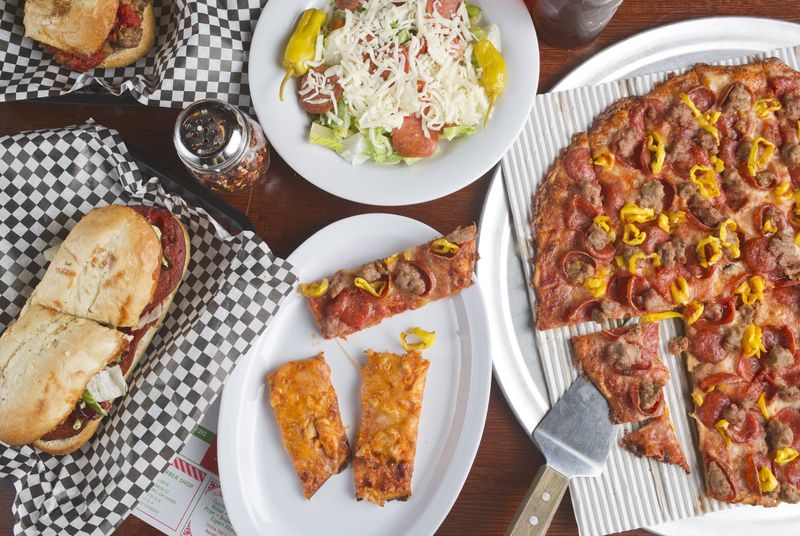 Clockwise from left: an Italian sub, a meatball sub, a side salad and a large pizza with pepperoni, sausage and banana peppers plus two slices of the Buffalo chicken pizza at Vick's Gourmet Pizzeria