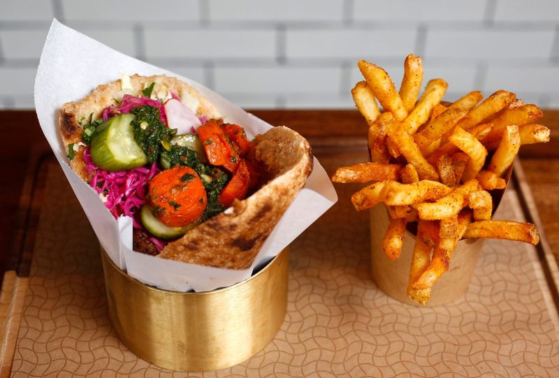A sandwich filled with hummus, greens, brisket, pickled cabbage, cucumbers, radishes and spicy carrots, served with a side of Brassica fries that are sprinkled with paprika and sumac.