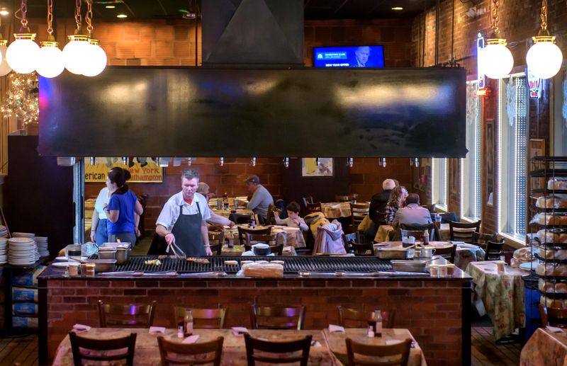 Blake Beason, a chef at Alexander's Steakhouse, works the grill while other customers choose their steaks from a nearby refrigerator at the popular Peoria restaurant. Customers can choose to make their own or let the restaurant's experts do the cooking.