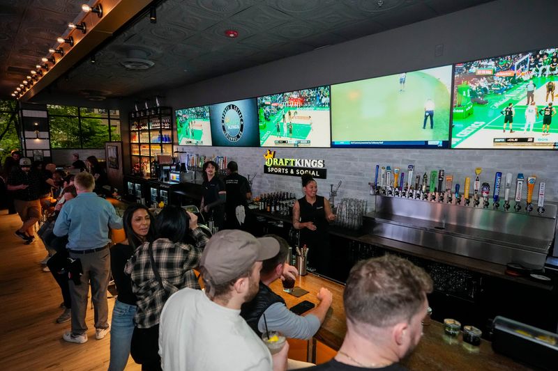 Sports are shown on TVs behind the bar as guests enjoy the grand opening of DraftKings Sports & Social in Columbus in 2024.
