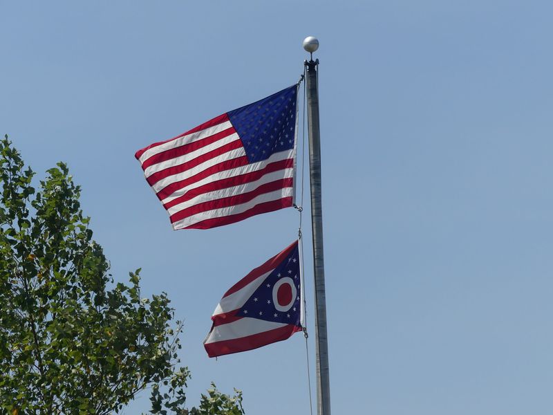 The American and Ohio flag wave on a pole.