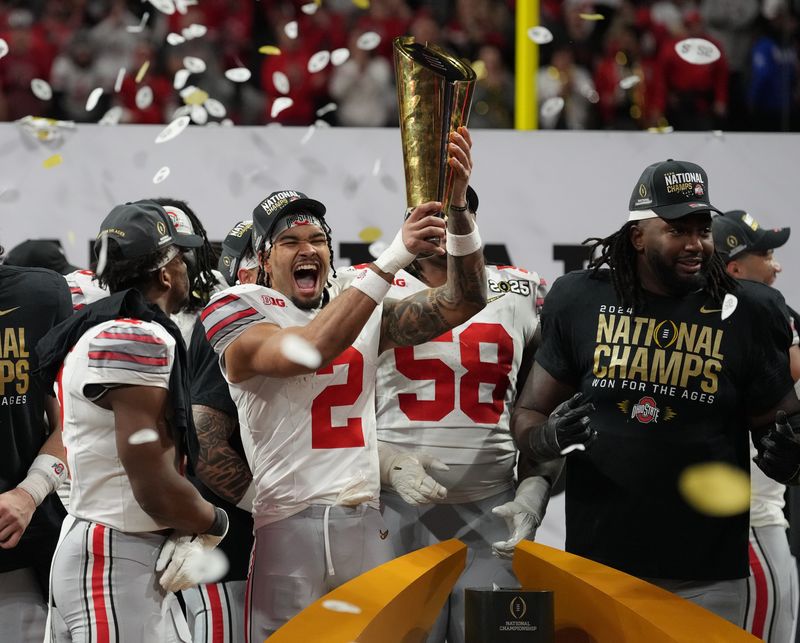 Jan 20, 2025; Atlanta, GA, USA; Ohio State Buckeyes safety Caleb Downs (2) hoists the CFP National Championship trophy after defeating the Notre Dame Fighting Irish in the CFP National Championship college football game at Mercedes-Benz Stadium. Mandatory Credit: Kirby Lee-Imagn Images