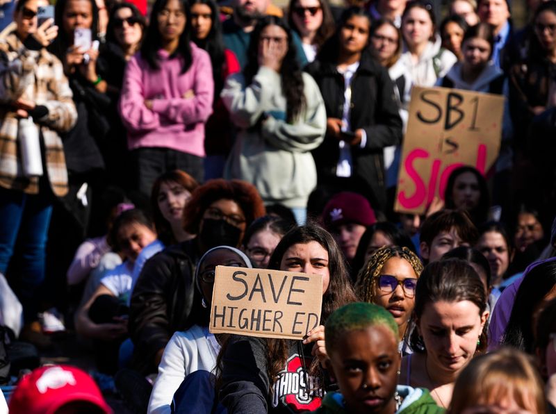 A woman holds a sign that says, “SAVE HIGHER ED” during a protest over Senate Bill 1 at The Oval on the campus of Ohio State University on Tuesday, March 4, 2025 in Columbus, Ohio.