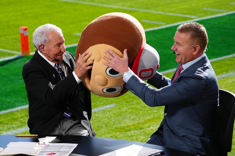 Jan 1, 2025; Pasadena, California, USA; Lee Corso (left) wears a Buckeyes mascot head as Kirk Herbstreit watches at Rose Bowl Stadium. Mandatory Credit: Kirby Lee-Imagn Images