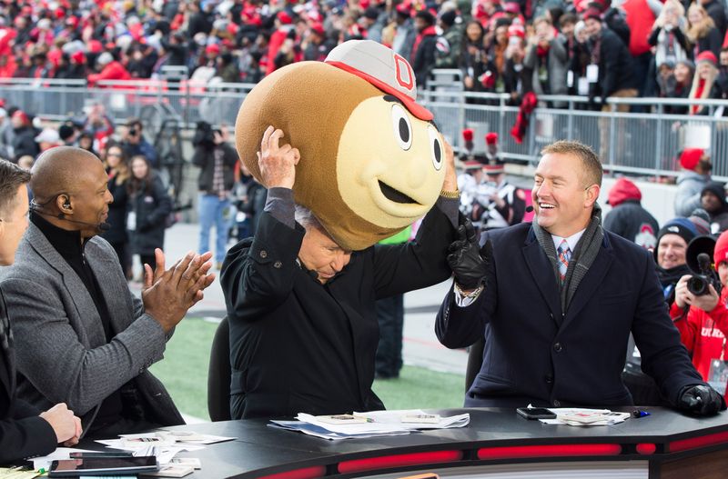 Nov 23, 2019; Columbus, OH, USA; ESPN Gameday host Lee Corso puts on a Brutus Buckeye head on while sitting between former Buckeyes Eddie George and Kirk Herbstreit before the game between the Ohio State Buckeyes and Penn State Nittany Lions at Ohio Stadium. Mandatory Credit: Greg Bartram-USA TODAY Sports
