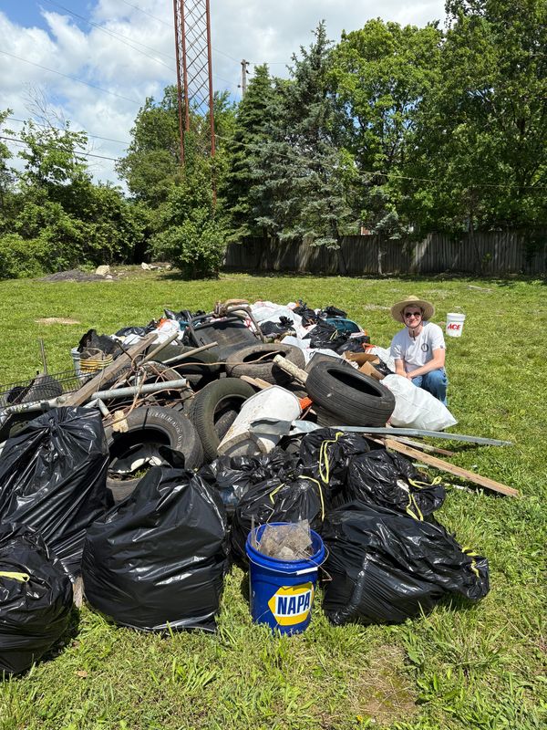 Collin Marshall is shown next to a pile of trash and tires. In the first three months of work, the group disposed of over 12,000 pounds of trash.