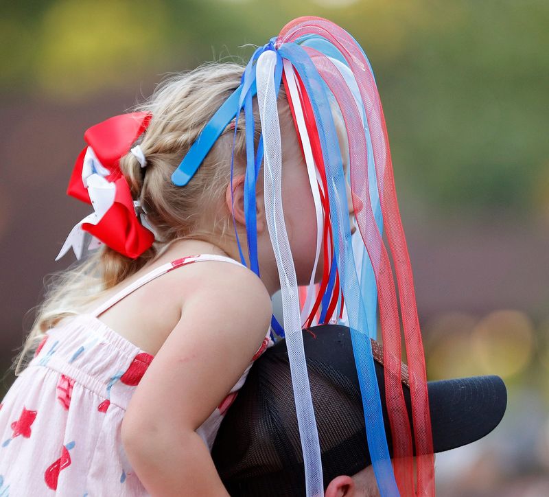 Ryleigh Mills, 4, of East Canton, sits atop her dad Matt's shoulders as she peeks through festive streamers Friday, July 4, 2025, at Silver Park in Alliance during the city's annual holiday celebration.