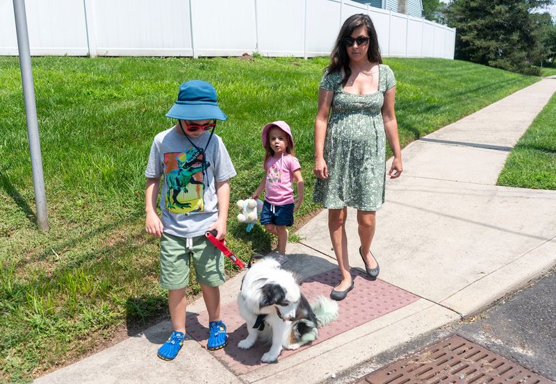 Lincoln Bergey, 8, left, who has a visual impairment and autism, waits at the corner with his service dog, Marley, a miniature Australian Shepherd, sister, Alaina, 3, and mom, Tara Bergey, right, in Sellersville, Pennsylvania, on July 24, 2025.