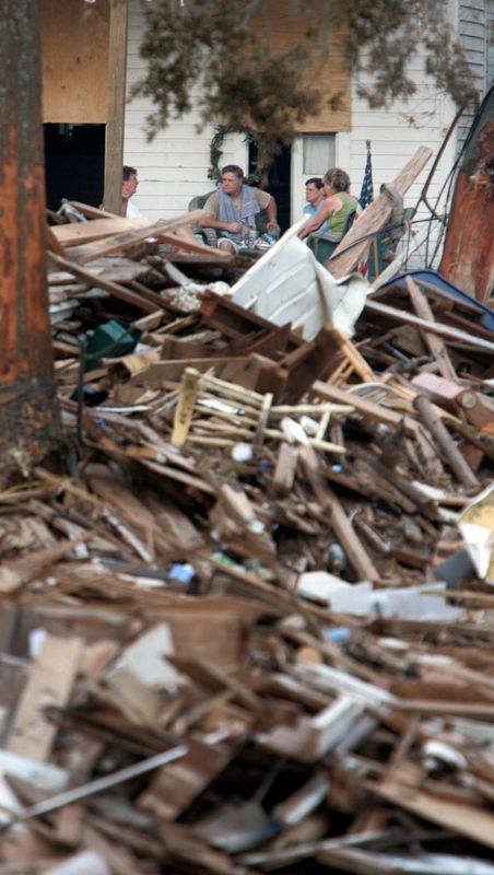 People gather on a front porch of a house near a pile of debris and wreckage in Biloxi, Miss., on Sept, 2, 2005.