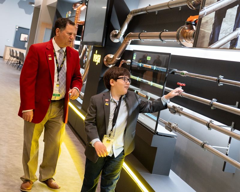 Rocco Fana, chapter director of Plumbing-Heating-Cooling Contractors of Ohio, looks on Thursday, Sept. 4, 2025, as his son, Sawyer, 9, checks out an interactive lobby wall design at Viega North America’s new carbon-neutral, $178 million manufacturing facility and training center in Shalersville.