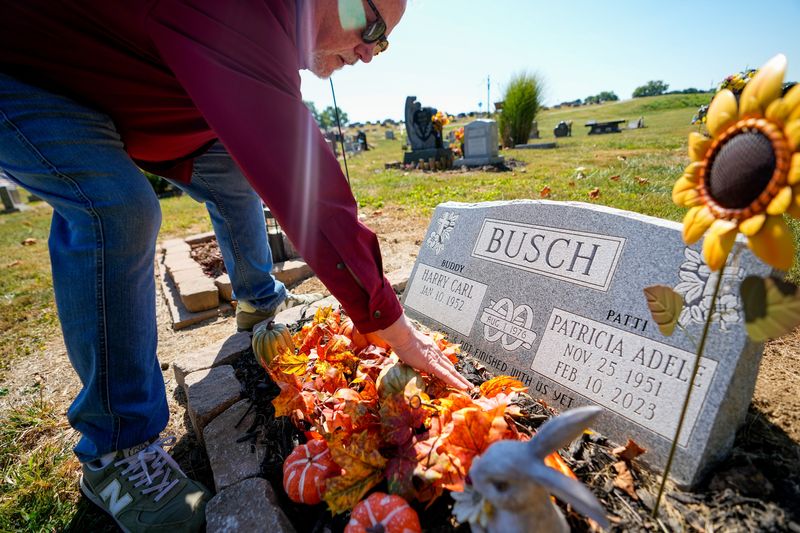 Buddy Busch adjusts the decorations by the headstone of Patricia Adele Busch at the Wilson Cemetery on Thursday, Sept. 11, 2025 in Newark, Ohio. Patti died of radon-induced lung cancer in 2023.